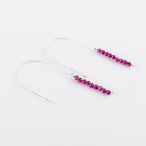 Puede incluir: Un par de pendientes de cadena de plata con una línea de cuentas de piedras preciosas rosas que cuelgan de cada cadena.