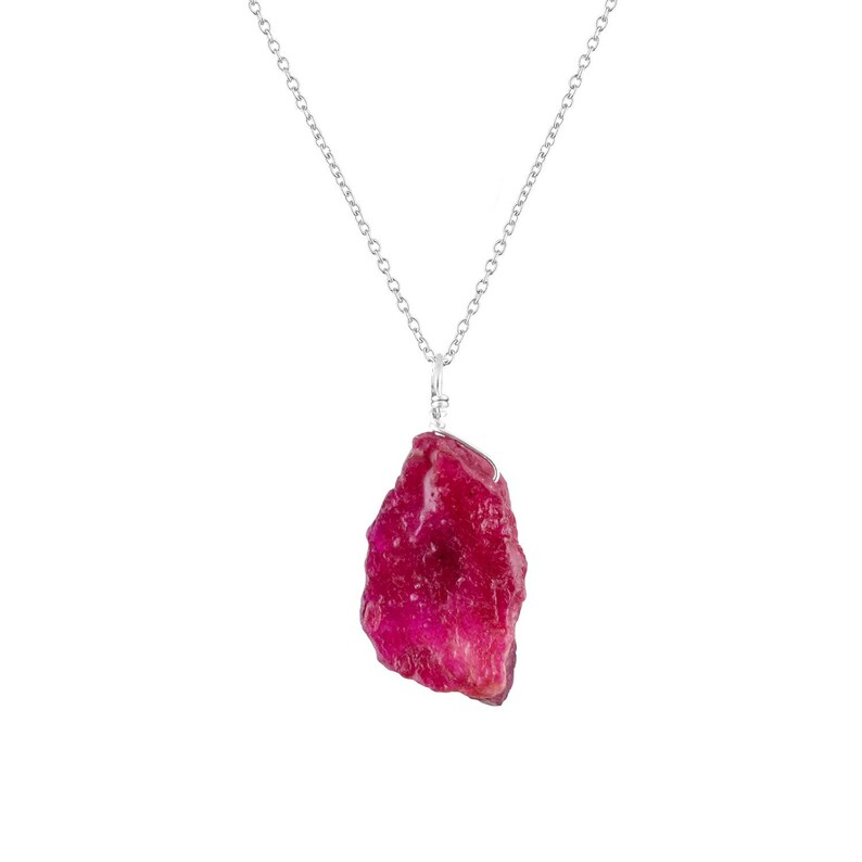 May include: A silver chain necklace with a large, raw ruby pendant. The ruby is a deep red color and has a rough, natural texture.