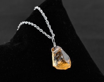 May include: A silver chain necklace with a raw, golden-brown crystal pendant. The crystal is faceted and has a rough, natural texture.