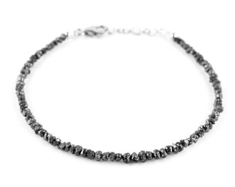May include: A delicate silver chain bracelet with a row of small, black, rough-cut diamonds.