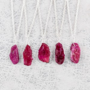 May include: Five silver necklaces with raw ruby pendants. Each pendant is a different shape and size, and they are all a deep red color.