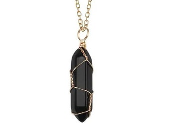 Puede incluir: Un collar de cadena dorada con un colgante de cristal negro. El colgante tiene forma hexagonal alargada, envuelto con alambre dorado. El collar se muestra sobre un fondo blanco.