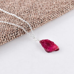 May include: A silver chain necklace with a raw, red ruby pendant. The ruby is a natural, irregular shape with a deep red color.