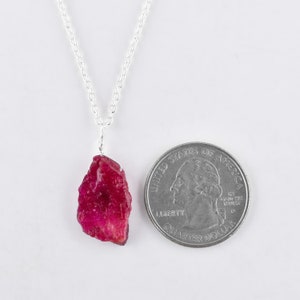 May include: A silver chain necklace with a raw ruby pendant. The ruby is a deep red color and is about the size of a US quarter.