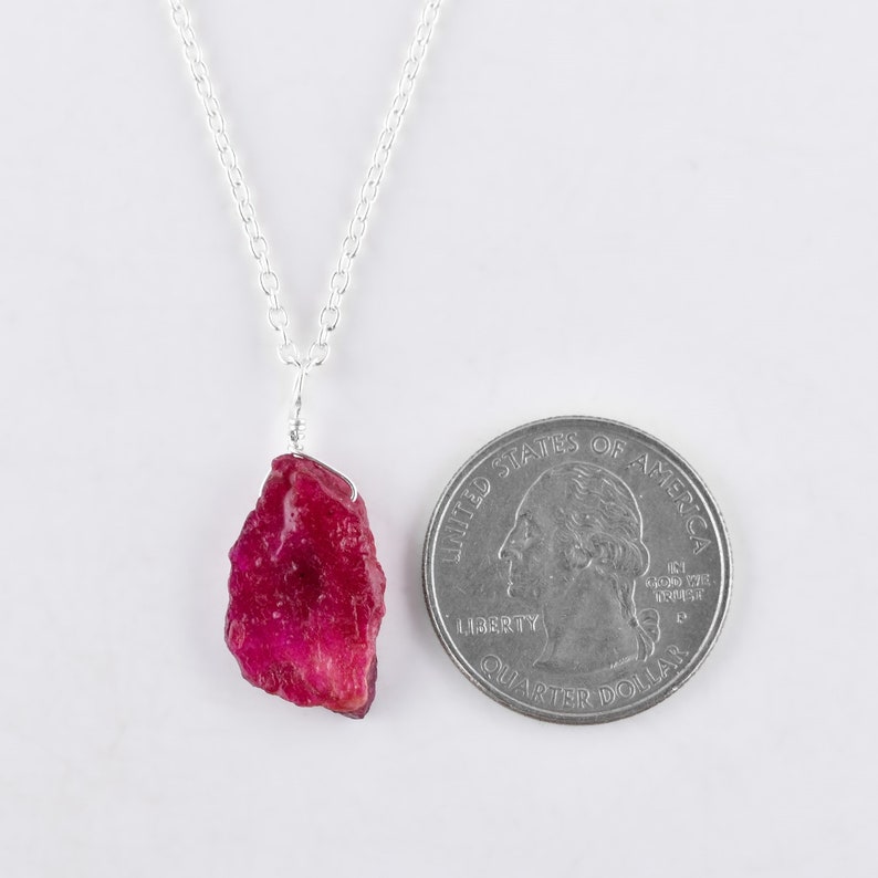 May include: A silver chain necklace with a raw ruby pendant. The ruby is a deep red color and is about the size of a US quarter.