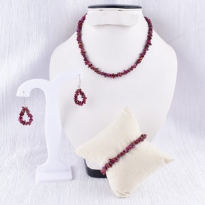 May include: A set of pink gemstone jewelry including a necklace, earrings, and a bracelet. The jewelry is displayed on a white stand and a white cushion.