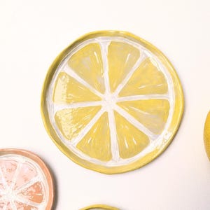 Può includere: Piatti in ceramica dipinti a mano a forma di fette di limone e arancia. I piatti sono gialli, bianchi e arancioni, con un design vivace. Ideali per servire snack o come elementi decorativi.
