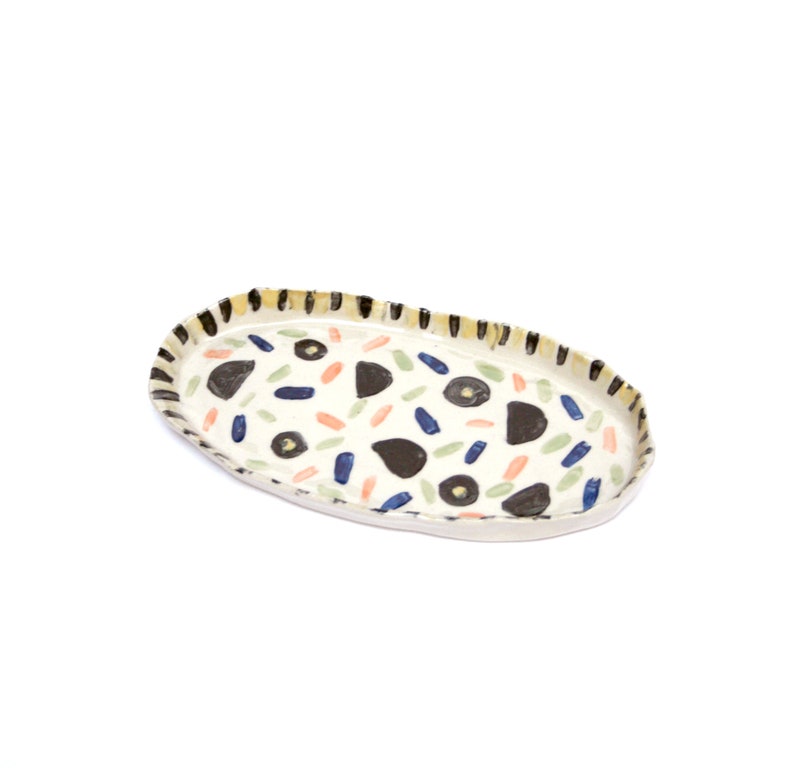 May include: White oval ceramic serving tray with a black, yellow, blue, green, and orange abstract pattern.