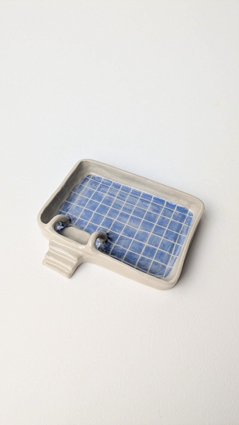 Puede incluir: Una bandeja rectangular de cer&aacute;mica con forma de piscina, con un borde gris claro y un patr&oacute;n de cuadr&iacute;cula azul y blanco en la base interior. La bandeja cuenta con una peque&ntilde;a escalera adjunta en un lado con tres pelda&ntilde;os horizontales.