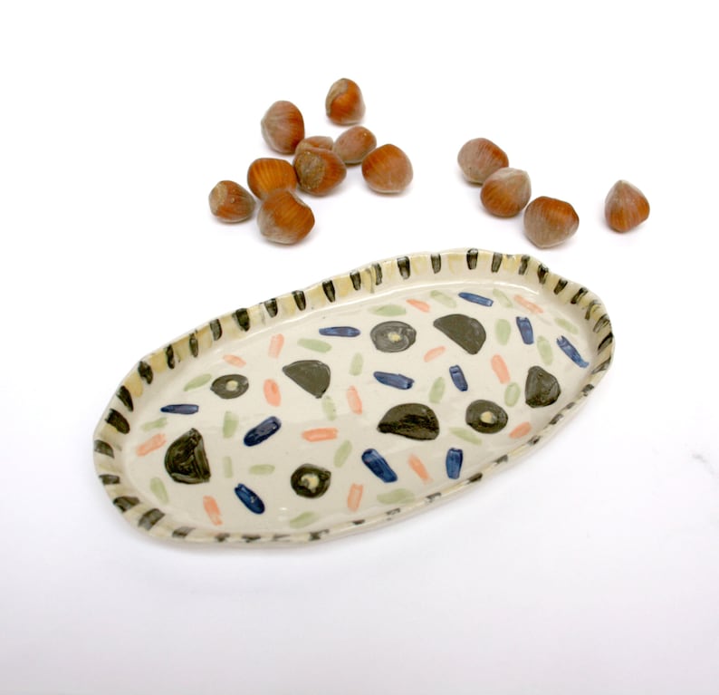 May include: A white ceramic oval serving dish with a black, blue, green, and orange abstract pattern.