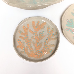 Puede incluir: Platos de cerámica hechos a mano con un diseño de arrecife de coral. Los platos son de color beige claro con coral naranja y puntos azules. Los platos tienen una forma orgánica y son perfectos para servir aperitivos o platos pequeños.