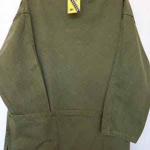 May include: An olive green long-sleeve shirt with a high collar and a large pocket across the lower back. A yellow rectangular tag is attached to the collar, featuring the text ALFREDSON ENGLAND in black lettering with a small logo graphic.