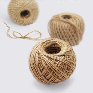 May include: Three balls of natural brown twine, made from jute, are shown on a white background. The twine is wound into balls and is ready to be used for crafts, packaging, or other projects.