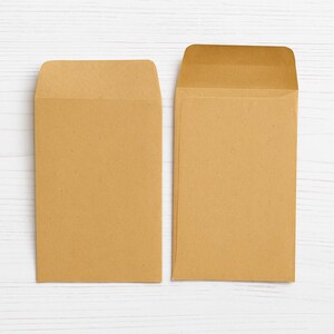 Puede incluir: Dos sobres rectangulares hechos de papel kraft de color marr&oacute;n claro. Un sobre se muestra con la solapa doblada hacia abajo, mientras que el otro sobre est&aacute; colocado con la solapa abierta, revelando la construcci&oacute;n interior de la papeler&iacute;a.