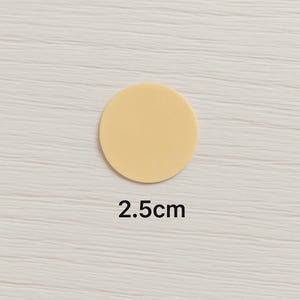 Puede incluir: Un disco circular de color amarillo p&aacute;lido s&oacute;lido con un acabado mate y liso. El objeto est&aacute; colocado sobre el texto 2.5cm, que indica su di&aacute;metro en unidades m&eacute;tricas. El disco es plano y presenta una superficie uniforme de color crema.