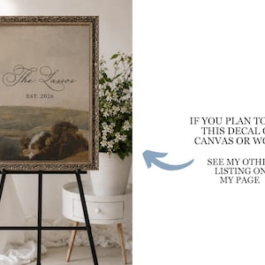 May include: An antique-style framed print on a black easel. The print features a landscape painting with the text "The Lassos EST. 2026". The frame has a gold finish. The image is displayed in a well-lit room with white flowers.