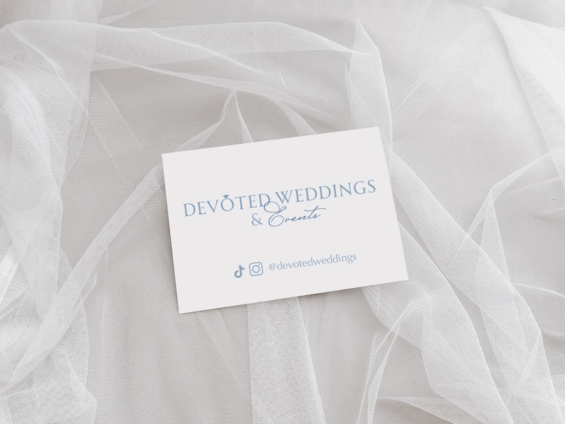 以下が含まれることがあります： 白地の名刺に、ソフトブルーのフォントで「DEVOTED WEDDINGS & Events」と書かれています。カードには、TikTokとInstagramのソーシャルメディアアイコンと、ハンドル名@devotedweddingsも含まれています。カードは白く透き通った生地の上に置かれています。