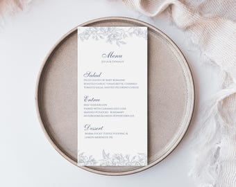 May include: A white wedding menu card with a floral border. The menu includes salad, entree, and dessert options. The text reads "Menu, Julia & Donald, Salad, Piled leaves of baby romaine, Roasted garlic vinaigrette, Charred tomato salsa, Shaved picorino cheese, Entree, Beef tenderloin, Paired with caramelized leeks, Mashed potatoes, Rosemary mushrooms & green peppercorn jus, Dessert, Warm sticky toffee pudding & lemon meringue pie."
