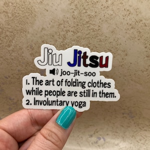 May include: A white sticker with the words "Jiu Jitsu" in colourful letters. The sticker also includes the pronunciation "joo-jit-soo" and a definition: "The art of folding clothes while people are still in them. Involuntary yoga."