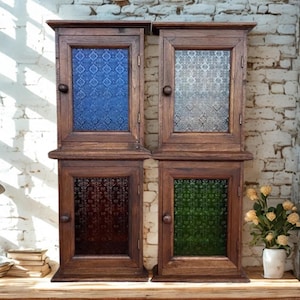 May include: Four wooden wall cabinets with glass doors. Each cabinet has a different colored glass panel: blue, clear, red, and green. The cabinets are made of dark wood and have a knob for opening the door. They are displayed on a wooden shelf.