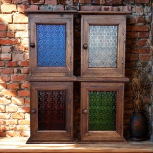 May include: Four rectangular wooden wall cabinets arranged in a two-by-two grid. Each cabinet features a single door with a central glass panel. The glass panels are textured with a repeating pattern and come in blue, clear, dark red, and green.