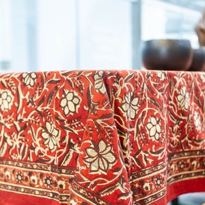 May include: Red tablecloth with a floral pattern. The tablecloth has a border with a smaller floral pattern. The tablecloth is made of cotton and is perfect for a dining table.