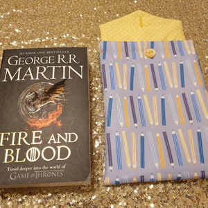 以下が含まれることがあります： ジョージ・R・R・マーティンによるベストセラー「炎と血」というタイトルの本。表紙にはドラゴンが描かれている。この本は、黄色、青、紫の鉛筆の模様がついた紫と青のブックカバーに入っている。