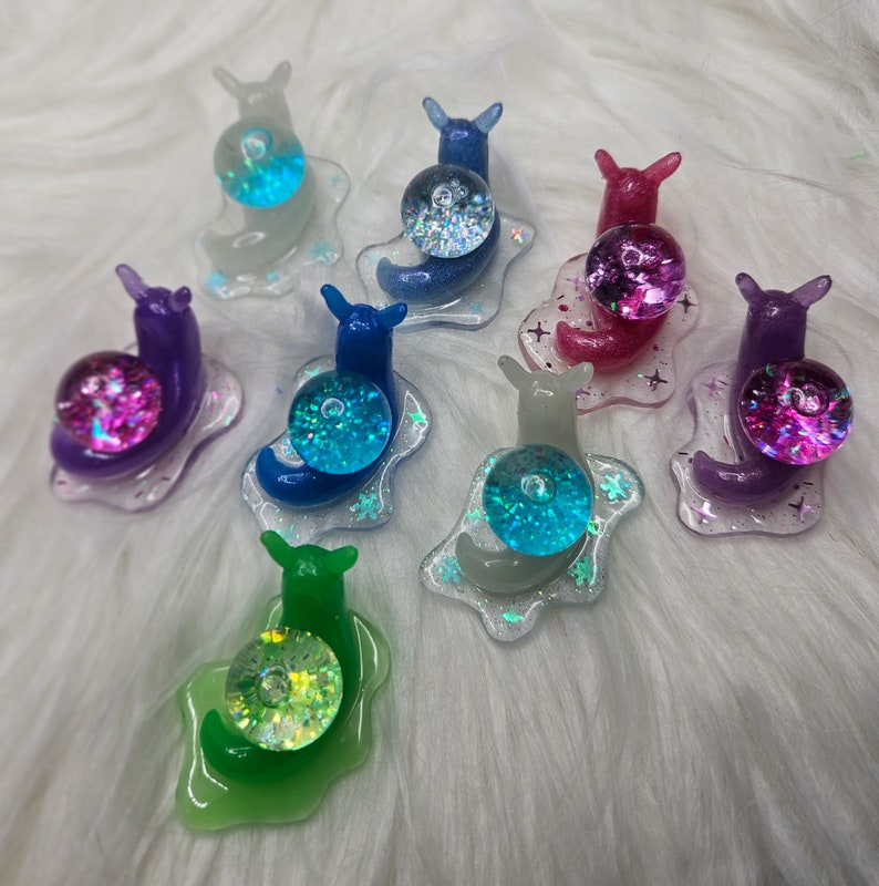 May include: Assortment of ten colorful snail charms with iridescent glitter accents. Each snail charm features a different color and glitter combination.