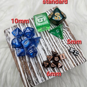 May include: Assorted dice sets in various colors and sizes, including blue, green, and bronze. The dice are displayed on a white and brown wooden surface. Sizes include 10mm, 6mm, and 5mm. The word "standard" is also visible.