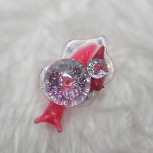 May include: A pink and white resin snail charm with a clear, glittery dome and a pink butterfly accent. The snail has a detailed shell and a whimsical design.