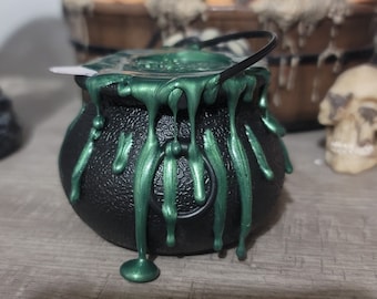 Può includere: Un calderone nero con cera verde che cola, una decorazione di Halloween.