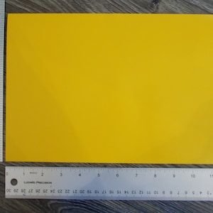 May include: A solid yellow sheet of paper, measuring approximately 11 inches by 8.5 inches, is placed on a wood grain surface.