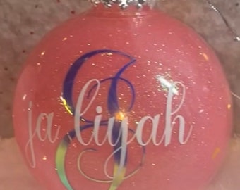 May include: Pink glitter Christmas ornament with the name "Ja'liyah" written in white lettering.