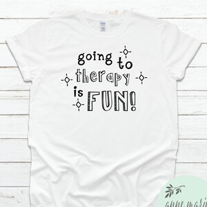 May include: White t-shirt with black text that reads "going to therapy is FUN!" with small diamond shapes around the text.