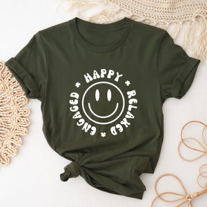 以下が含まれることがあります： 白いスマイリーと「Happy * Engaged * Relaxed *」というテキストが書かれた緑色のTシャツです。