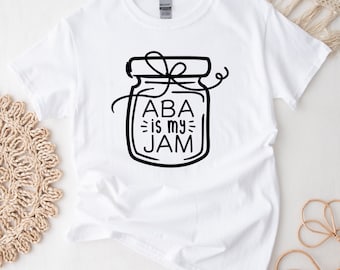 May include: White t-shirt with a black and white illustration of a jar with a lid and a bow. The text "ABA is my JAM" is inside the jar.