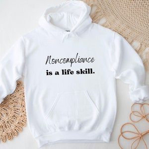 May include: White hooded sweatshirt with the text "Noncompliance is a life skill." printed in black.