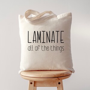 May include: A white canvas tote bag with black text that reads "LAMINATE all of the things".