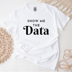 May include: White t-shirt with black text that reads "Show Me The Data" in a retro font.