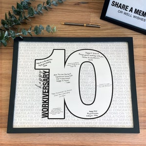 Może przedstawiać: Oprawiony wydruk przedstawiający dużą liczbę 10 z napisem WORKIVERSARY oraz odręcznymi wiadomościami od współpracowników. Tło stanowi powtarzający się wzór CONGRATULATIONS ON 10 YEARS OF SERVICE. Rama jest czarna i prostokątna.