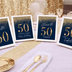 Op de afbeelding: Vier ingelijste marineblauwe en gouden 50e verjaardagsborden. Elk bord heeft een witte rand en bevat gouden tekst met zinnen als "Hello 50", "50 Years Loved", "Cheers to 50 Years" en "50 and Fabulous".