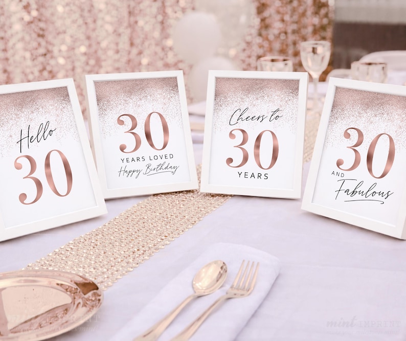 May include: Four framed signs with the number 30 in rose gold, with phrases like "Hello 30" and "Cheers to 30". The signs are on a table with gold cutlery and a decorative runner, perfect for a birthday celebration.