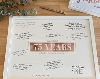 May include: A white framed guest book with a rose gold inscription that reads "75 Years" and a white background with handwritten messages. The inscription is surrounded by a white border.