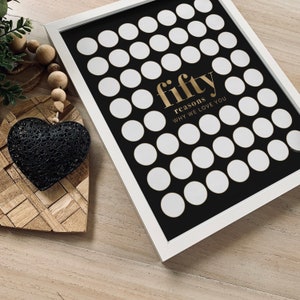 May include: A white framed black and white print with 50 white circles arranged in a grid pattern. The text "fifty reasons why we love you" is written in gold lettering.