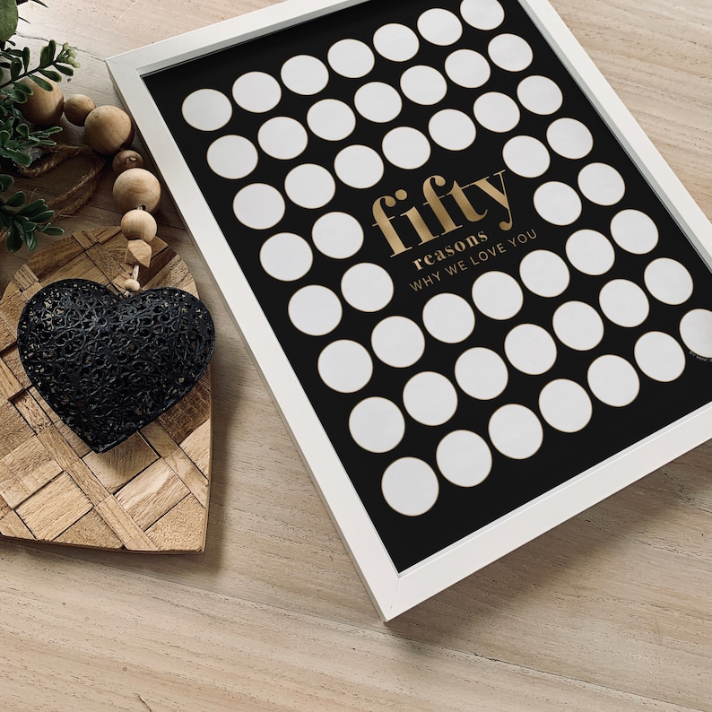 May include: A white framed black and white print with 50 white circles arranged in a grid pattern. The text "fifty reasons why we love you" is written in gold lettering.