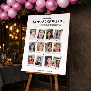 Op de afbeelding: Een wit bord op een houten ezel, ter viering van "60 JAAR OLIVIA". Het bord bevat twaalf foto's en de tekst "LAAT ONS ZIEN HOE JE HET VERJAARDAGSMEISJE ZULT KENNEN, RAAD WELKE LEEFTIJD ZE OP ELKE FOTO HAD, WIE DE MEESTE JUISTE HEEFT!" Roze ballonnen zijn op de achtergrond.