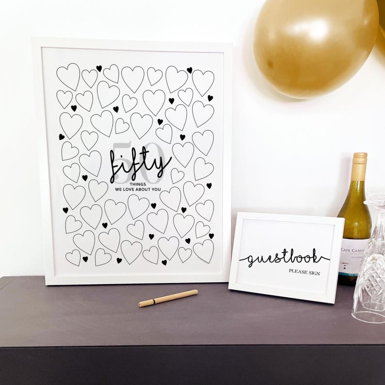 50th Birthday Party Sign In for Guests to write 50 birthday messages in the blank hearts, displayed in white frame with gold balloons, wine, glassware and a small sign that reads Guestbook Please Sign