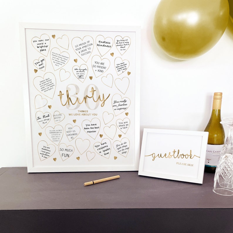 30th Birthday Sign made as a digital printable download for 30th Birthday Decoration to match Gold Party Supplies. Displayed on a black table in two white picture frames, with pen for Guests to write their heartfelt nostalgics messages for the 50 Year Old Woman.