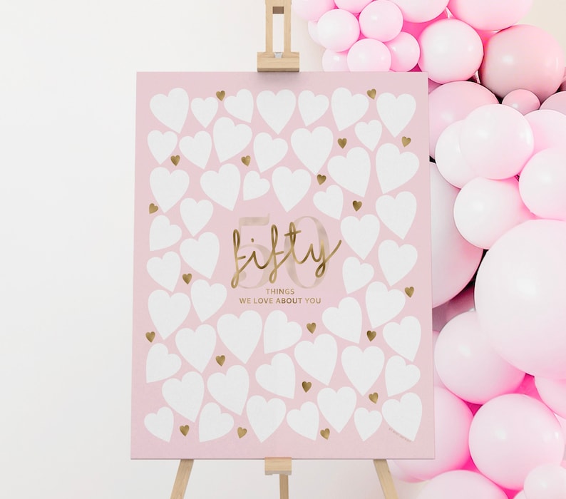 May include: Pink and gold sign with 50 white hearts and the text "fifty things we love about you".