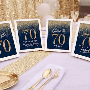 May include: Four framed navy blue and gold 70th birthday signs. Each sign has a white border and features gold text with phrases like "Hello 70", "70 Years Loved", "Cheers to 70 Years", and "70 and Fabulous".